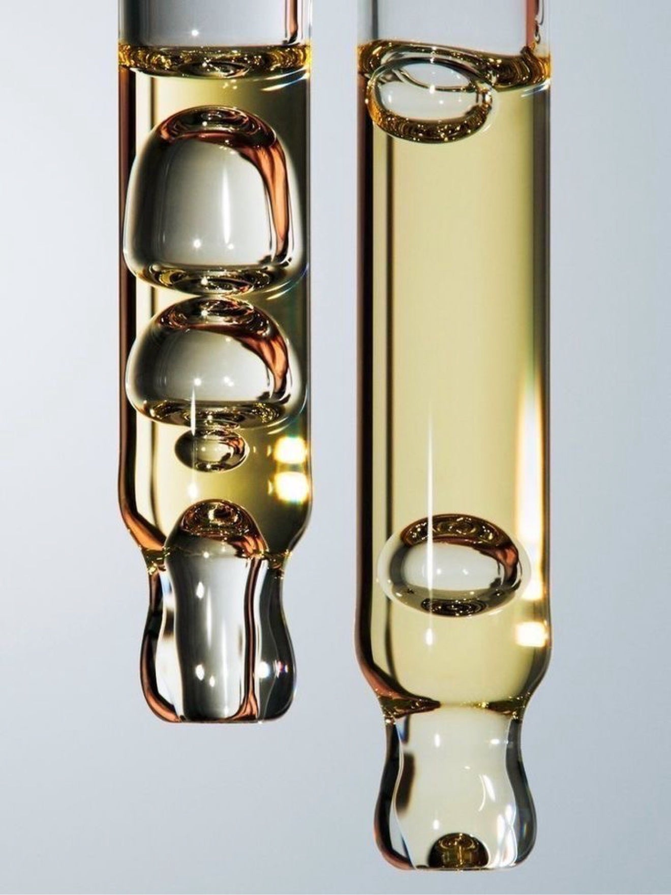 Glass pipettes filled with golden MelaBODY oil, bubbles suspended inside