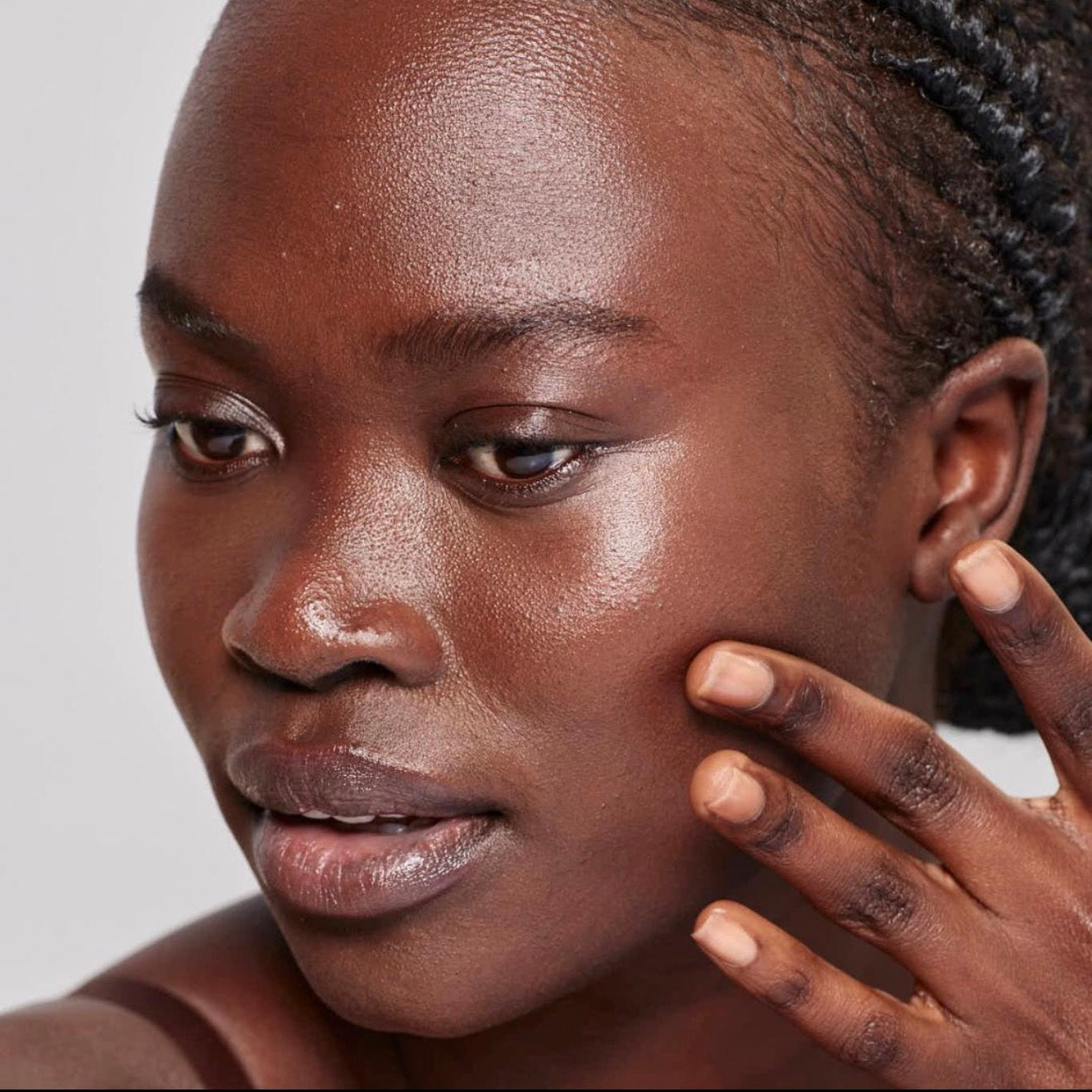 Portrait of a woman with deep brown, luminous skin, hand resting on her cheek