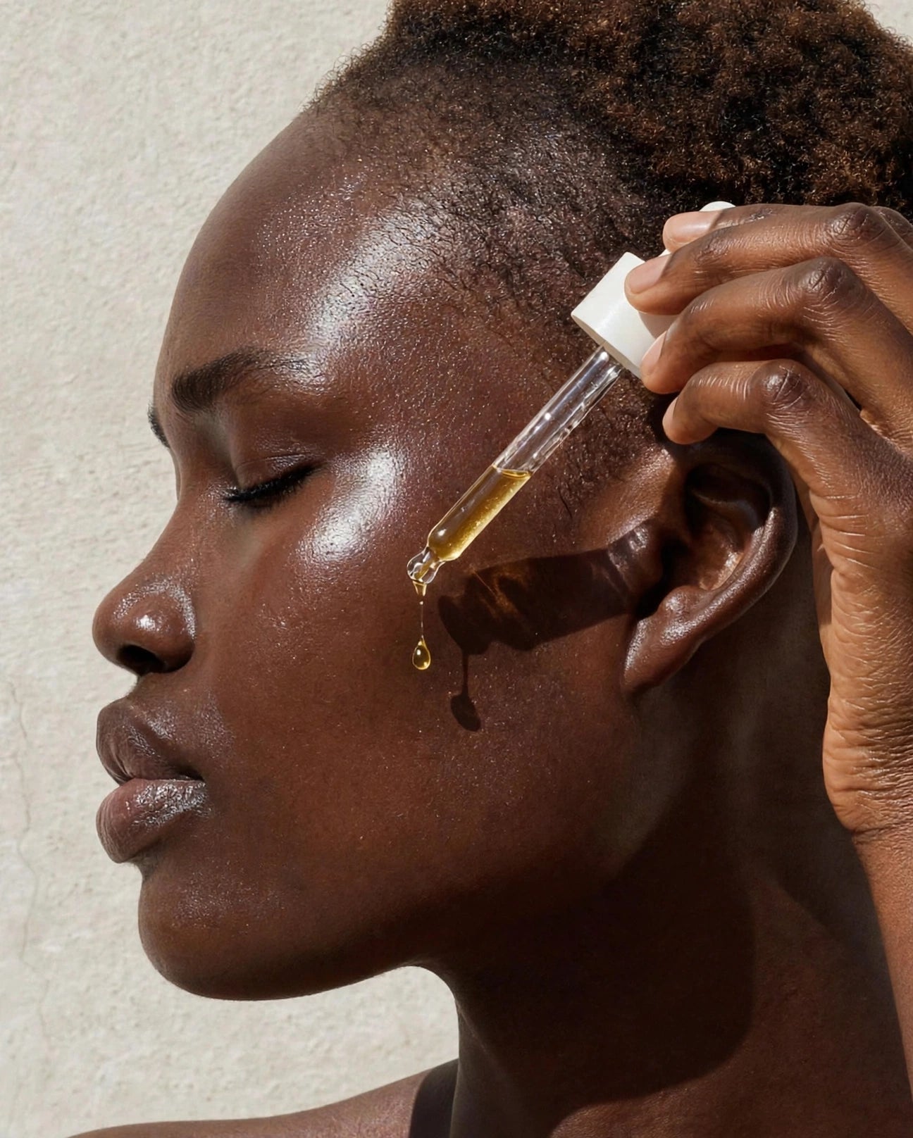 Dropper applying golden serum to rich brown skin